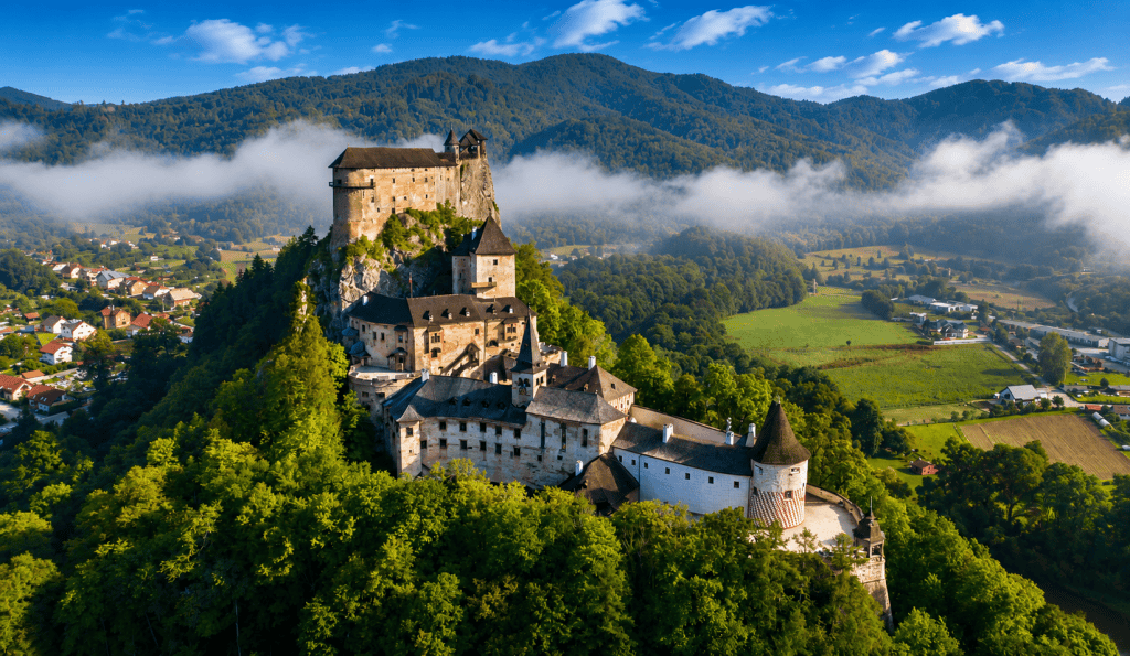 Aerial view of Orava Castle above misty village and hills