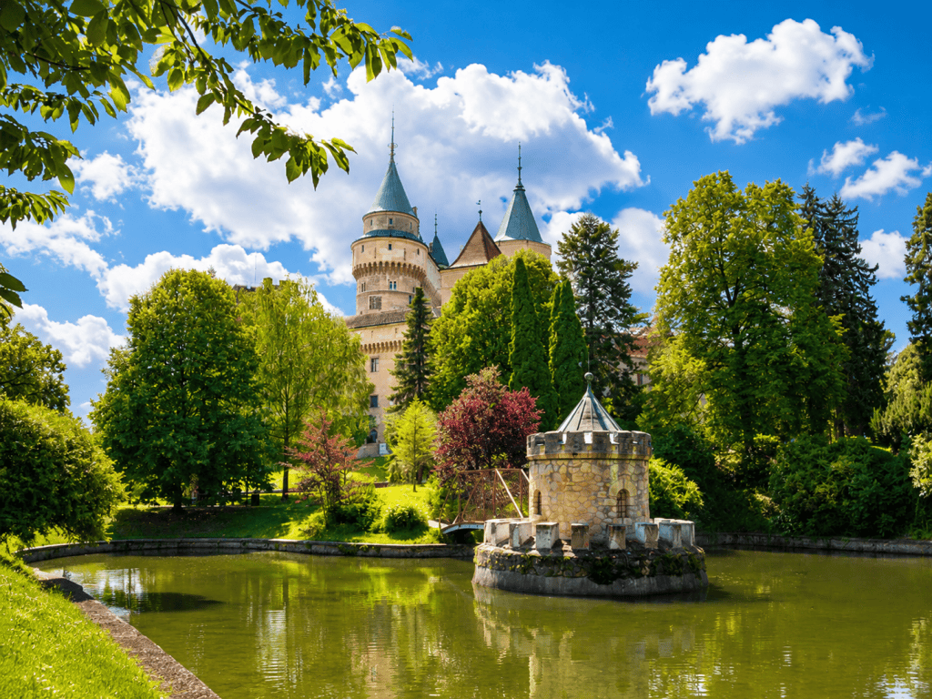 Bojnice Castle towers behind pond in landscaped park