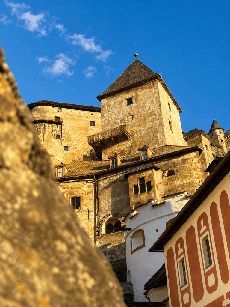Stone towers of Orava Castle glowing in golden evening light