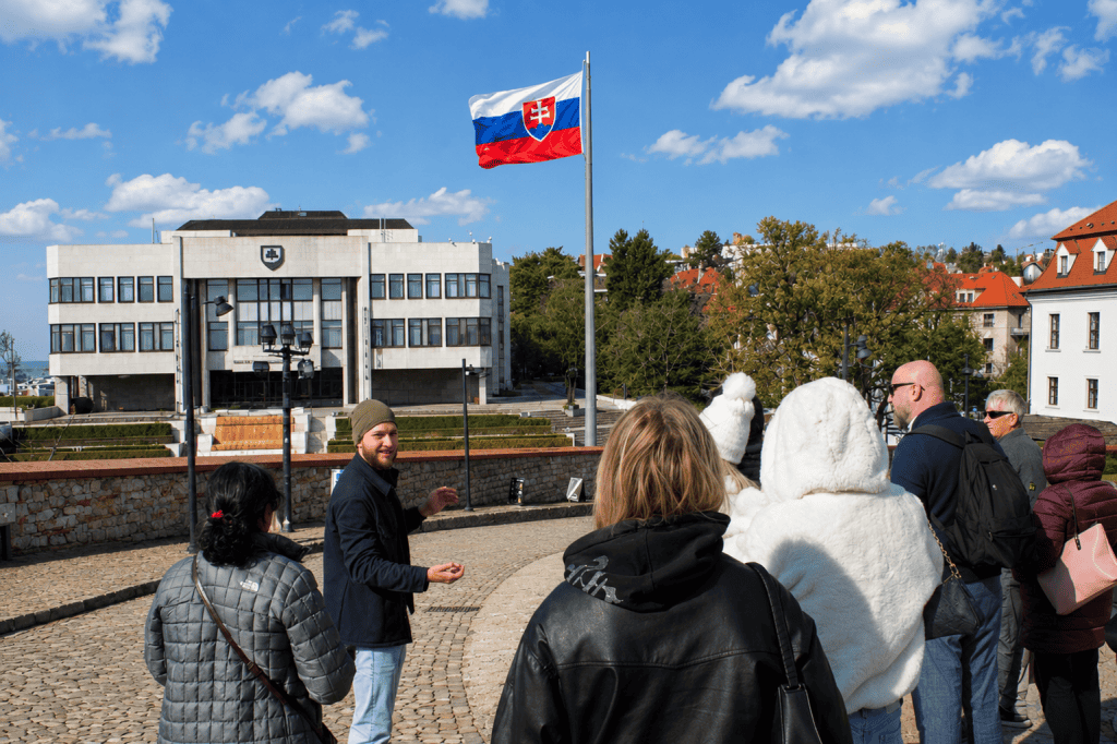 Tour group with guide near Slovak parliament and flag in Bratislava